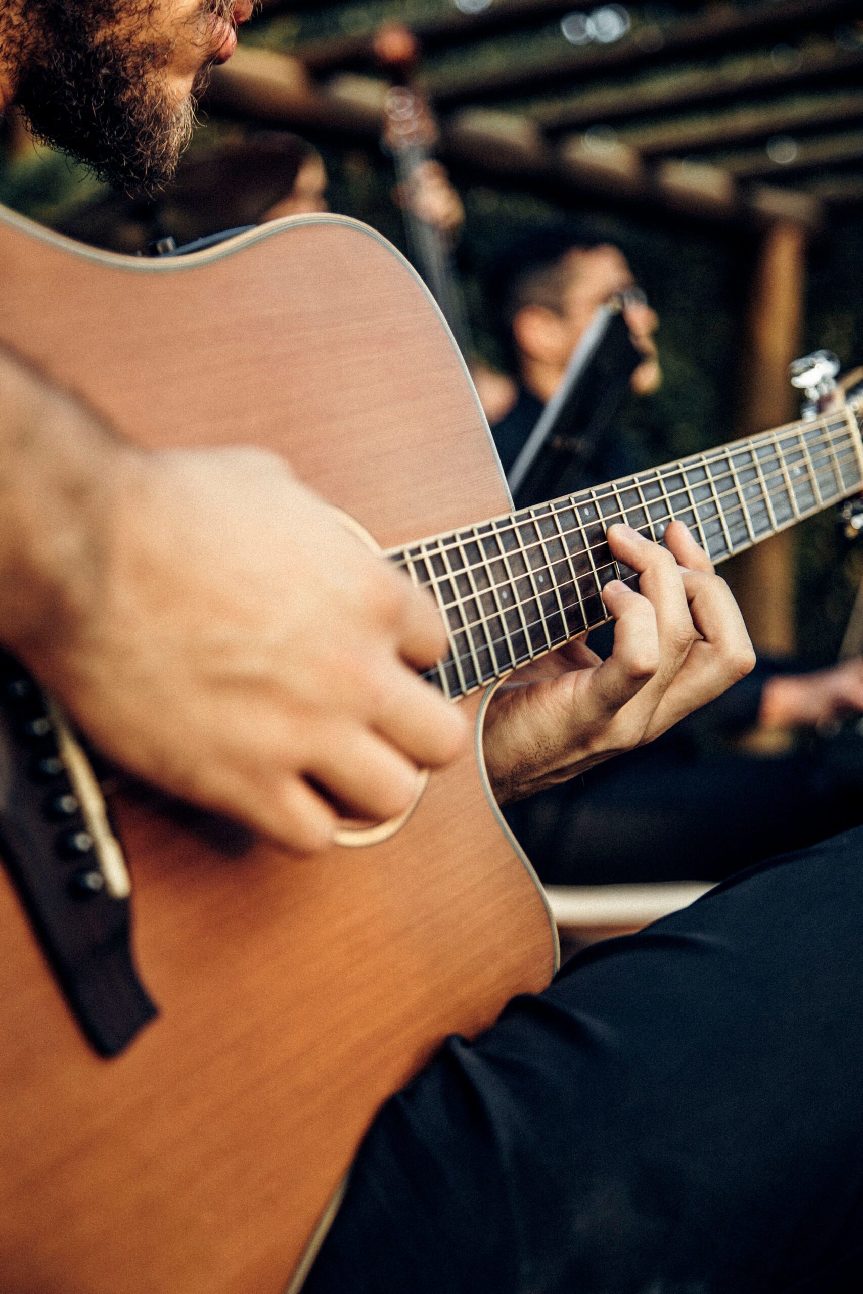 A close-up shot of a man strumming an acoustic guitar outdoors, emphasizing musical expression.